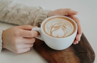 Latte in a white latte cup on a piece of dark wood; photo credit: Christiana Rivers / Unsplash