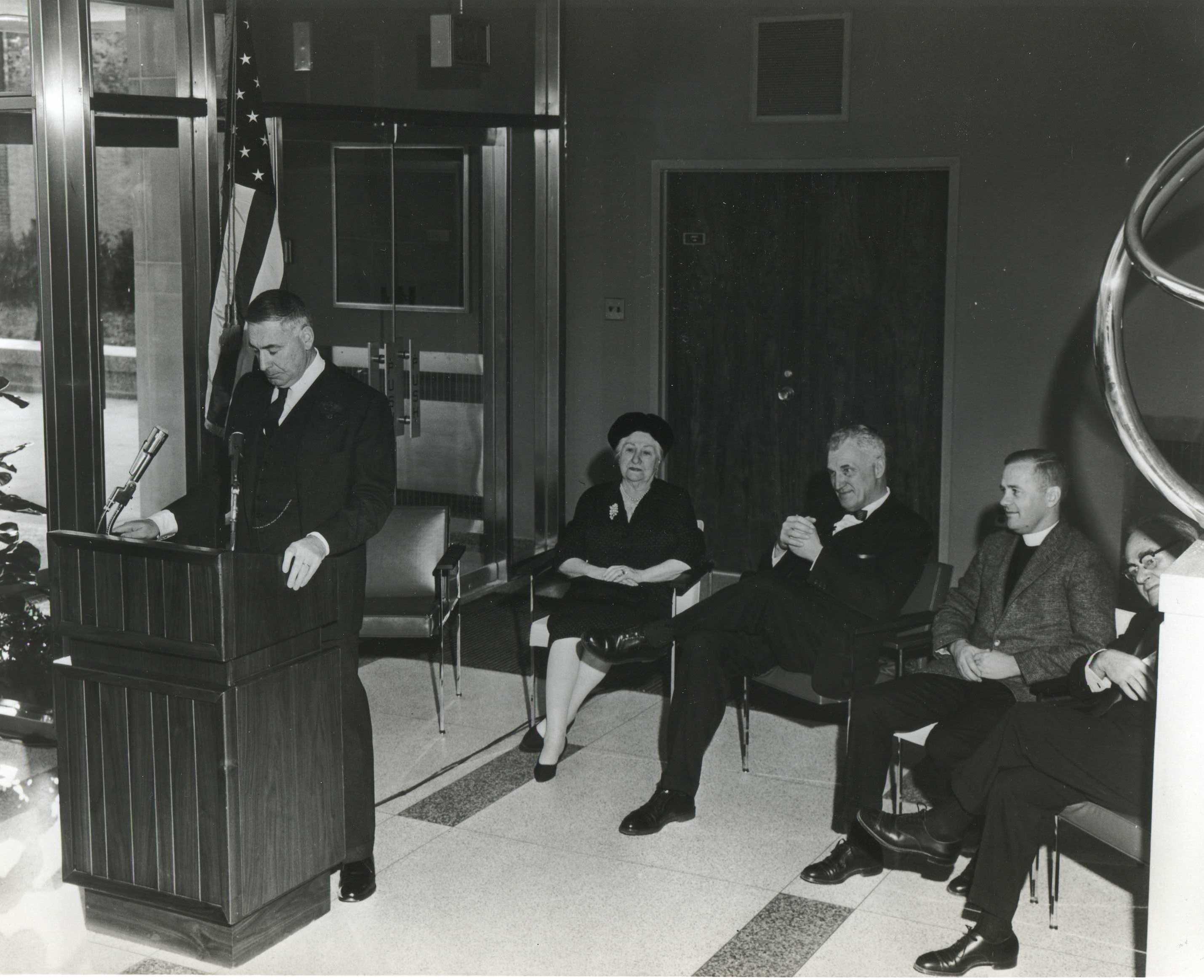 Walter Annenberg standing at a podium in 1960 with several people seated behind him
