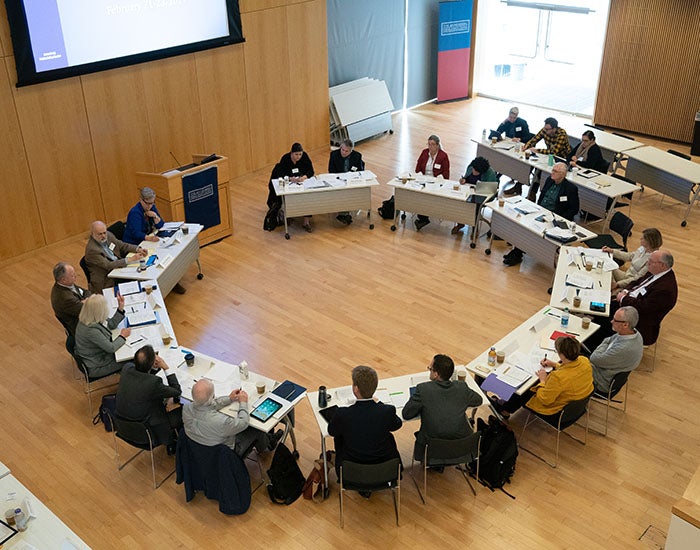 Circle of people sitting around desks in a large open room, viewed from high above