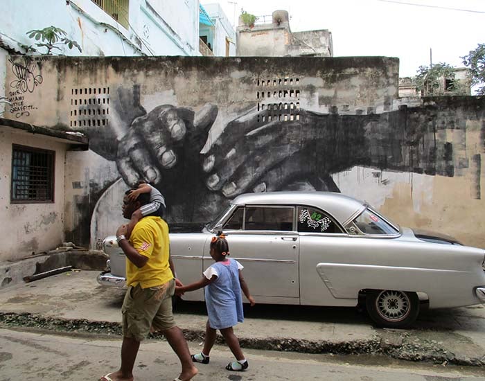 Mural showing hands with 1950s car in front of it and a man walking with a child on his shoulders while holding the hand of another