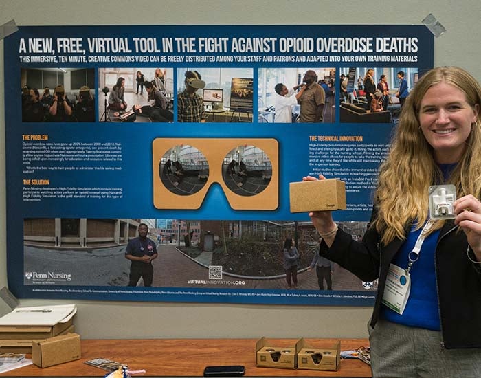 Woman holding Narcan and a Google cardboard standing in front of a poster with the headline &quot;A new, free, virtual tool in the fight against opioid overdose deaths&quot;