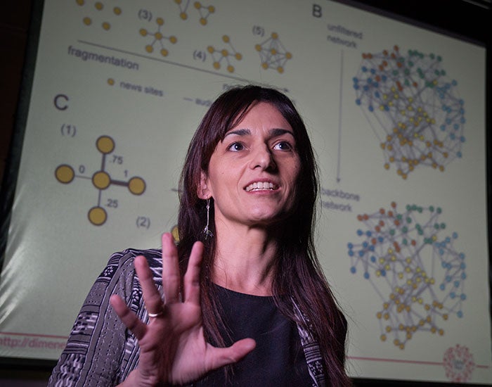 Sandra Gonzalez-Bailon standing front of a screen with many network diagrams