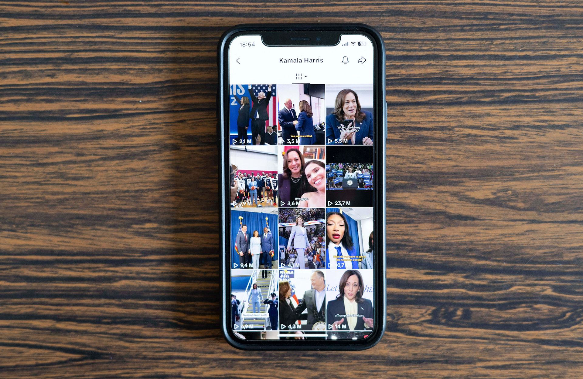 A cell phone showing TikTok videos of Kamala Harris sits on a wooden table