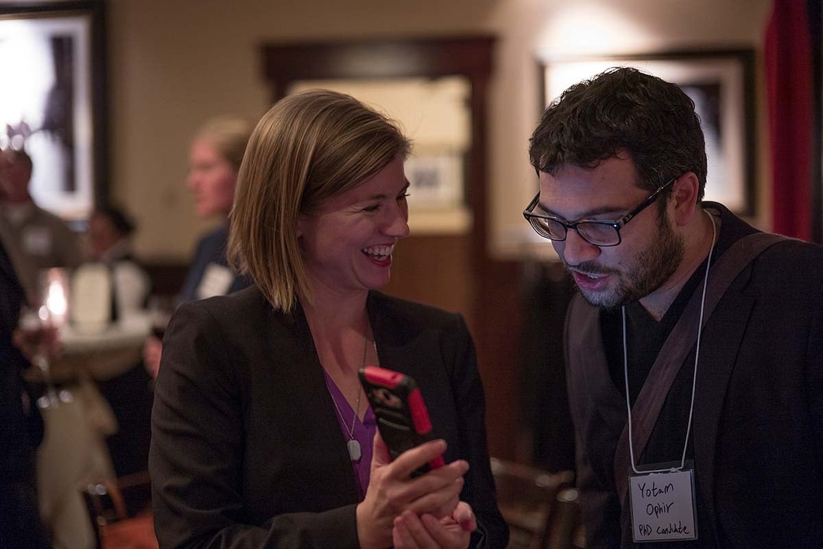 Holli Seitz laughing with Yotam Ophir as she shows him something on a phone