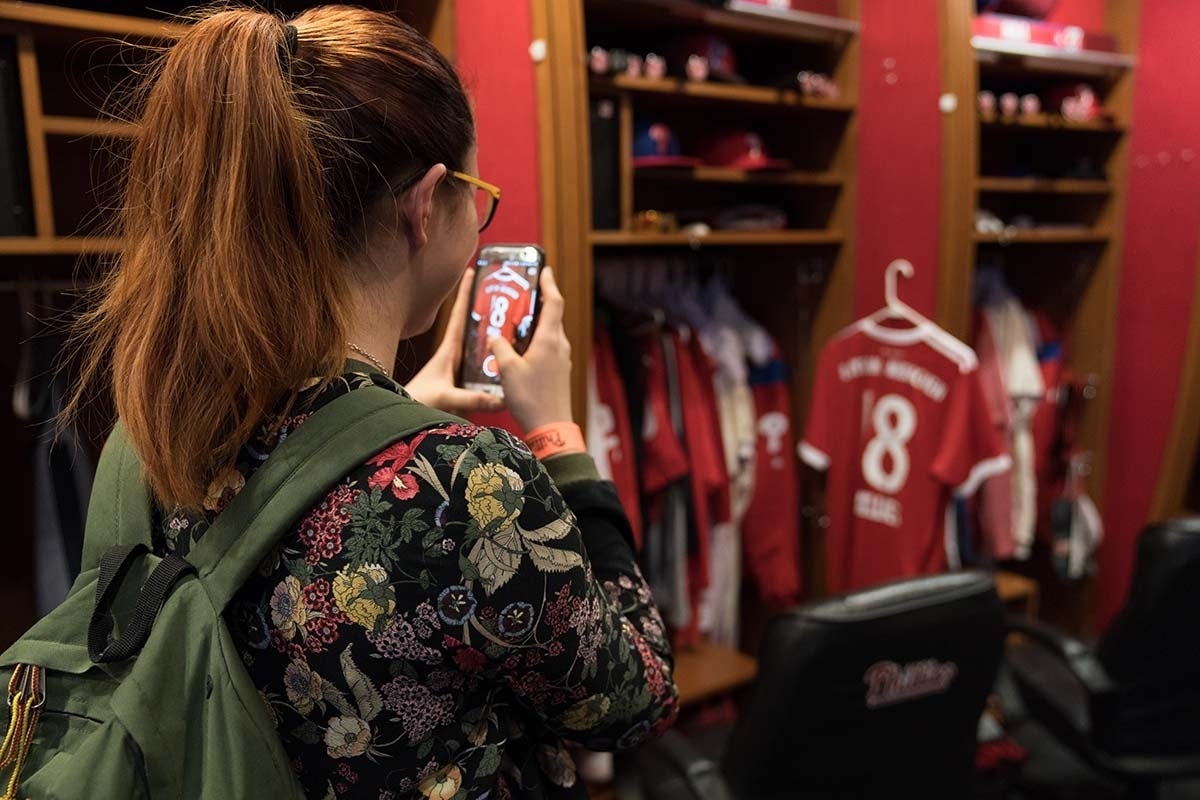 Student taking picture in the Phillies locker room, specifically of a red jersey with the number 18 on it