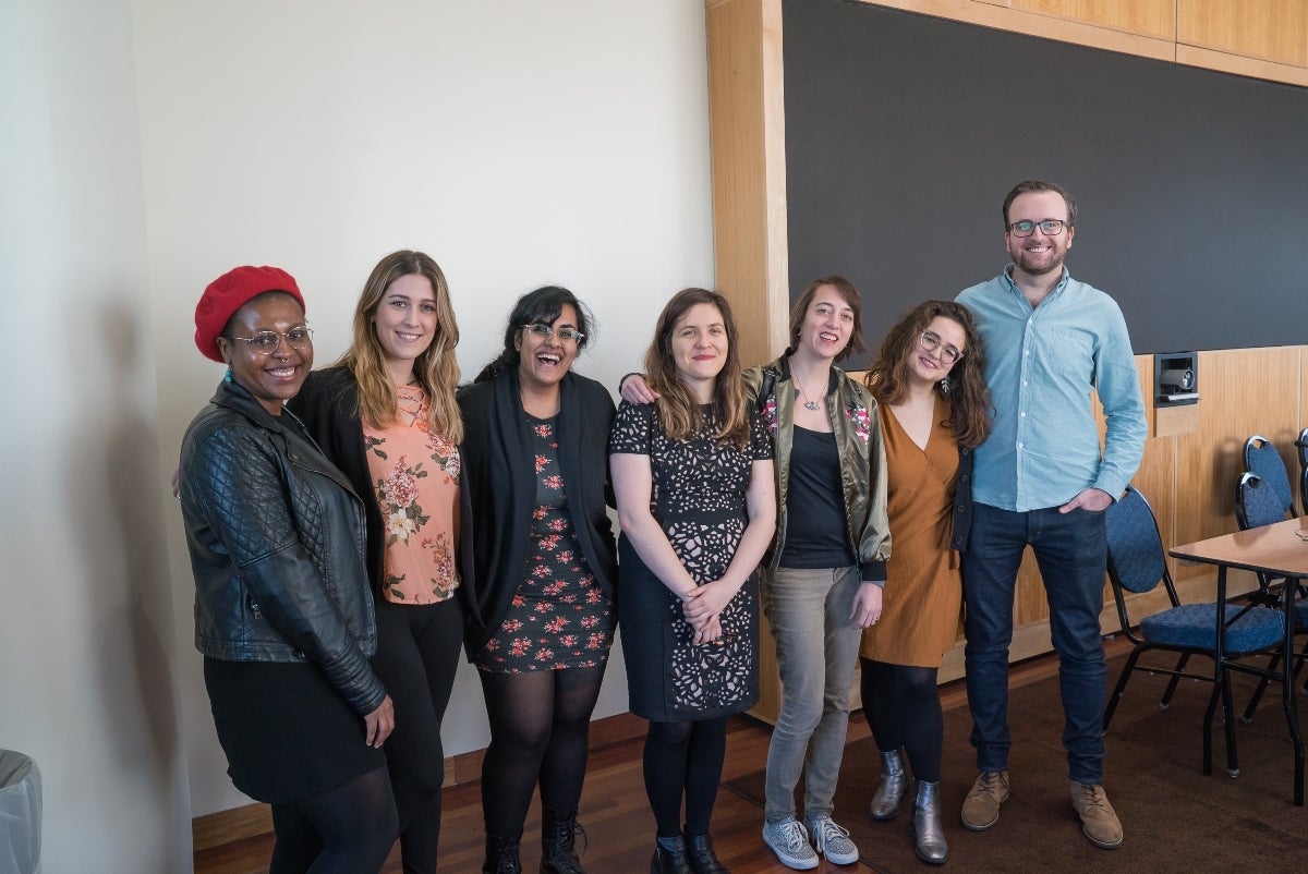 Florence Madenga, Jeanna Sybert, Roopa Vasudevan, Muira McCammon, Jessa Lingel, Isabelle Langrock and Zane Cooper posing in front of a white wall with a chalkboard to their left that is surrounded by wood. 