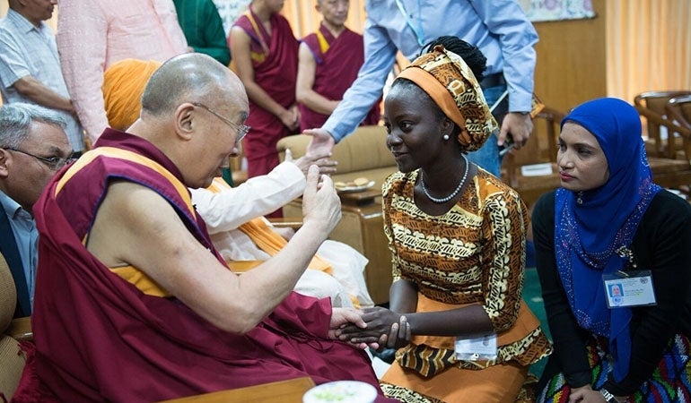 Side view of the Dalai Lama speaking with two young leaders who are in front of Him. They are listening attentively.  