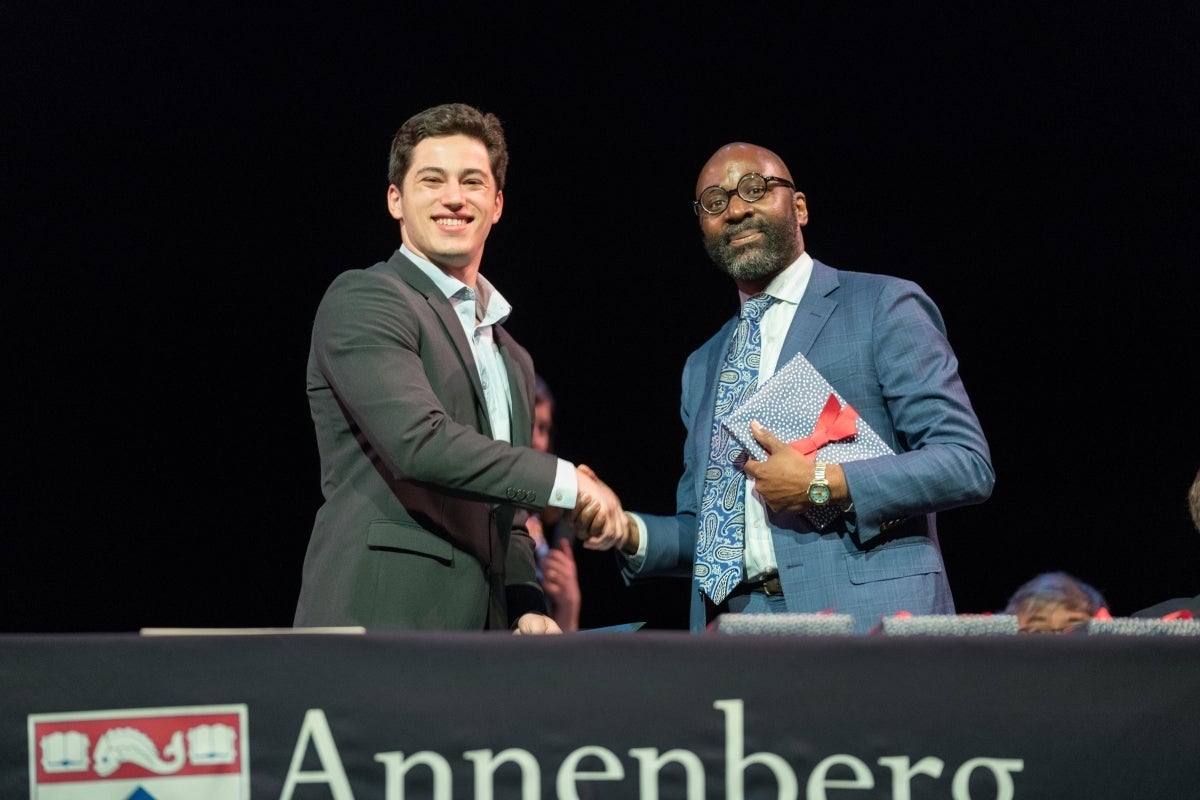 Ben Friedman smiling and shaking hands with Dean John L. Jackson, Jr. as he received an award which Jackson holds in his other hand. 