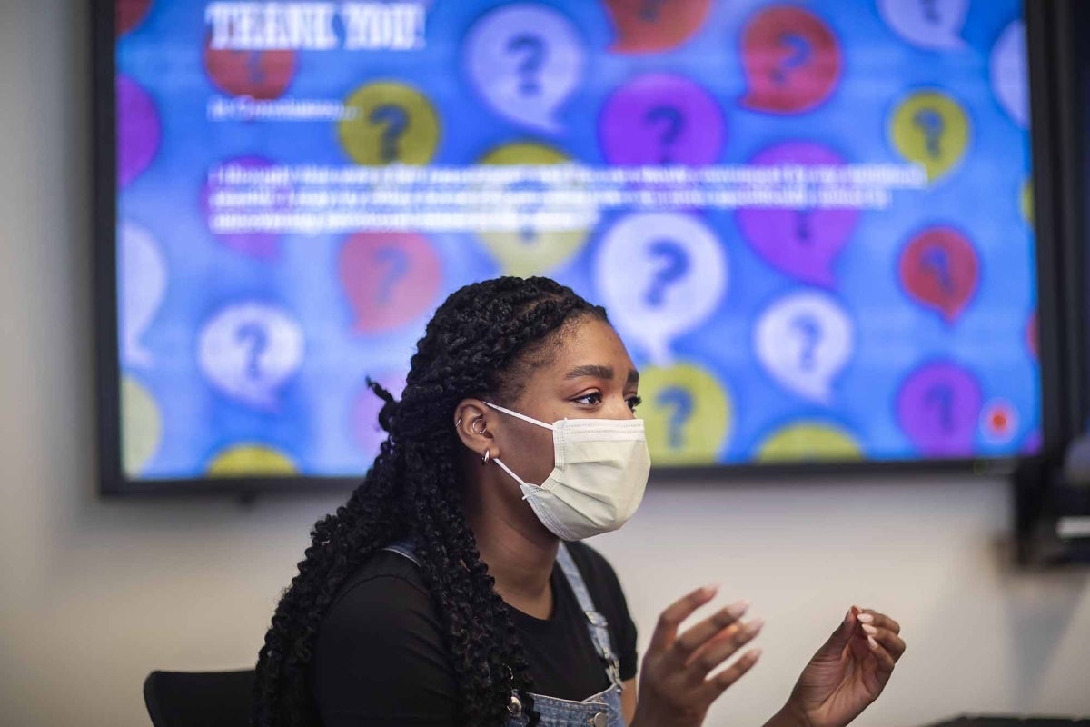 Adetobi Moses speaking with her hands-mid gesture and a colorful but illegible screen behind her