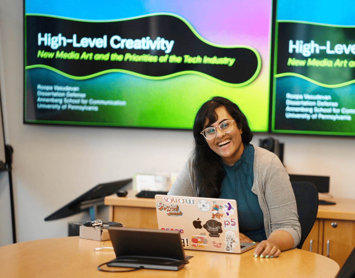 Roopa Vasudevan sits at a table in front of a laptop.