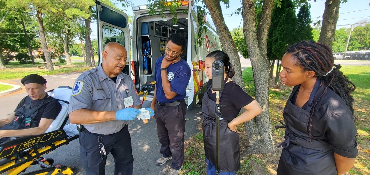 Real-life EMT Barry Hunter, second from left, talks to actors David Blatt, Newton Buchanan, Bi Jean Ngo, and Britt Fauzer. Blatt portrayed a man overdosing, Ngo and Fauzer acted as people administering Narcan, and Newton played an EMT. Kyle Cassidy, one of the creators of the training video, says Hunter helped teach Newton how to enter the scene and what to carry.