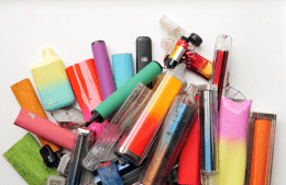 A collection of discarded electronic cigarette vapes and internal components shot over a white plastic background.