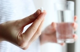 A woman holds a white pill and a glass of water