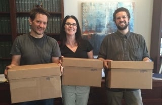 From left to right, Jeff Pooley, Laura Saywer and Jordan Mitchell smiling and posing with brown boxes in their hands