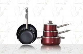 Front-view of a marble-tiled table with five pots and pans. On the right are three red shiny pots of different sizes stacked on top of each other, with the smallest on top with it's cover. On the left are two black frying pans with the face facing the front and the handles are upwards. The smaller one is in in front of the larger one. photo credit @cookerking / Unsplash