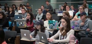 Students seated in a large classroom with laptops open in front of them