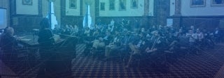 Audience in a large room listening to a woman speak at a podium