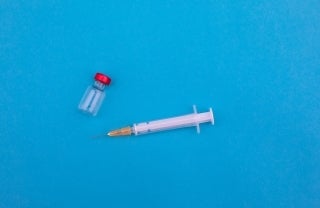 needle and vaccine bottle laying on a blue surface, photo credit Markus Spiske / Unsplash