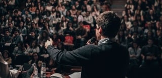 Man speaking in front of a large audience. Miguel Henriques / Unsplash