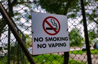 "No Smoking No Vaping" sign on a chainlink fence