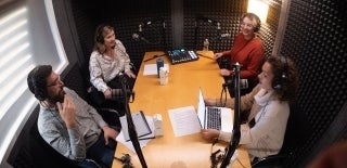 Four people sitting in a recording studio with microphones and computers