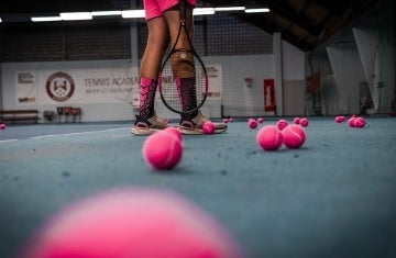 Legs shown with tennis racket surrounded by pink tennis balls