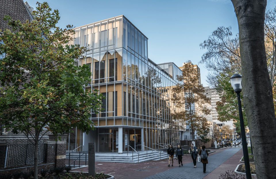 view of people walking past Annenberg Public Policy Center, a modern glass building, on a sunny day