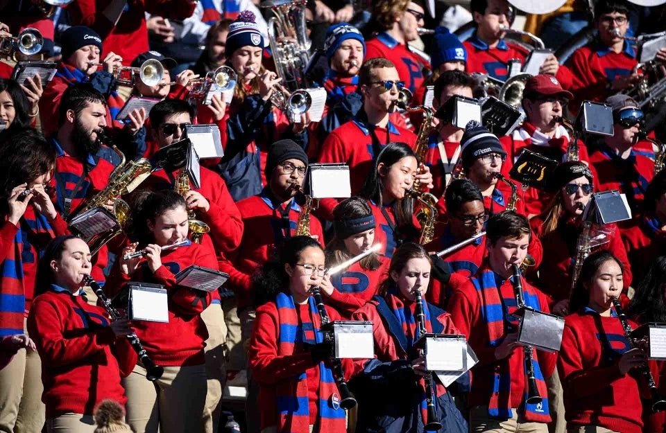 Penn marching band standing in the stands at a game, playing instruments