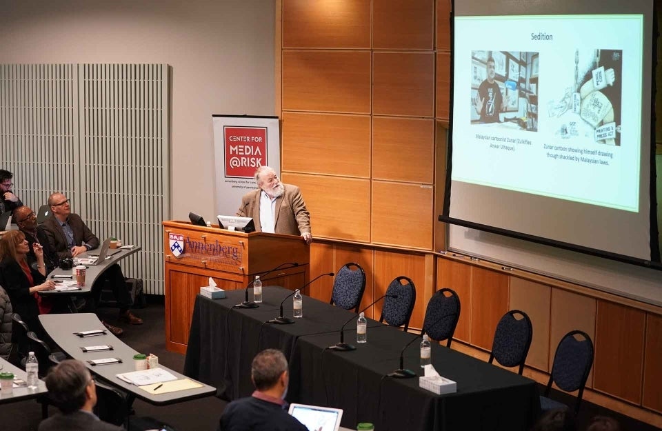 John Lent, standing behind a podium, giving a presentation to his audience in a lecture theatre