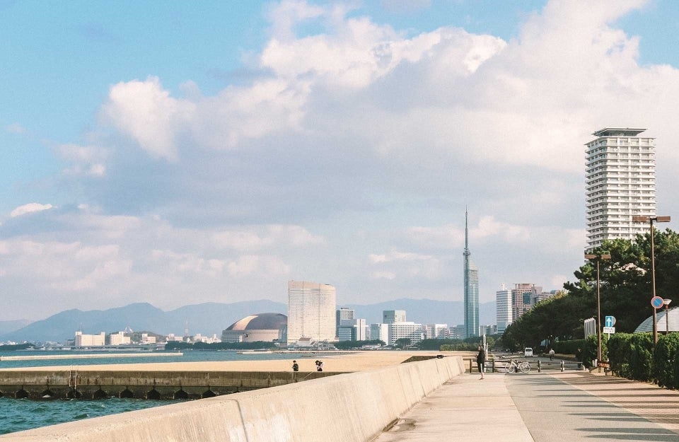 Picture of city in Japan, where to the left is a body of water and in front are buildings, photo credit @riverse / Unsplash