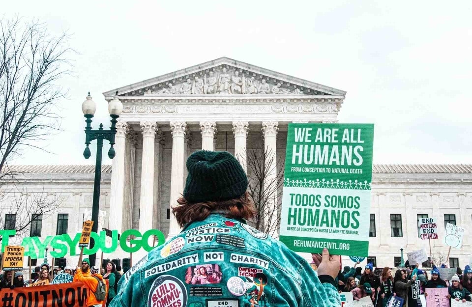 Sign reading we are all humans being held up in front of White House; photo credit: Maria Oswalt / Unsplash