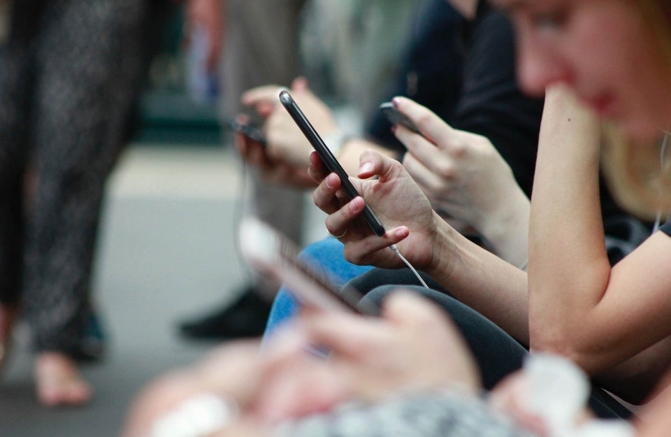 3 people on their phones, with the person in the middle in focus, in public area with surroundings blurred; photo credit: Robin Worrall / Unsplash