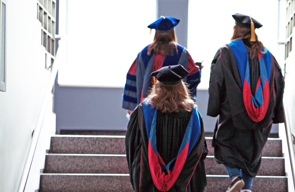 backs of graduates in cap and gown as they walk up the stairs