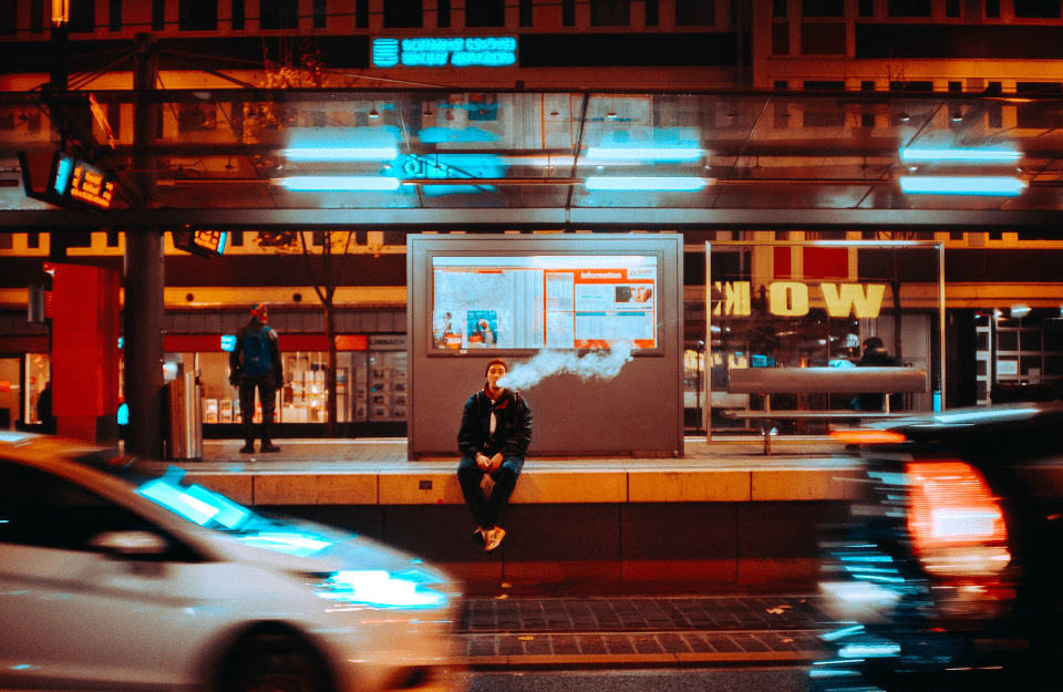 A man sits on a subway platform smoking an e-cigarette