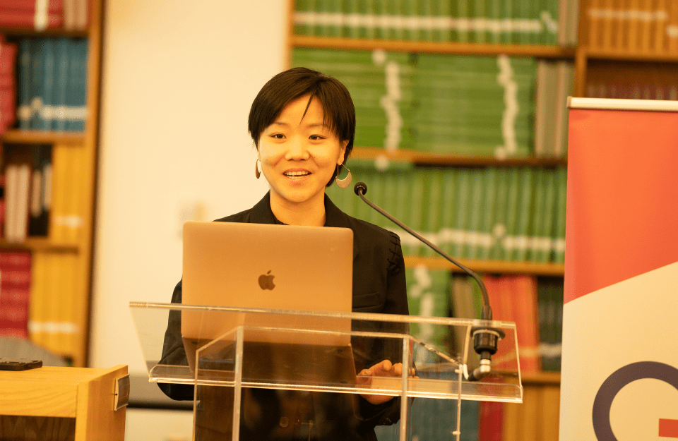 A woman stands at a podium and is speaking into a microphone