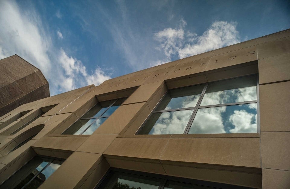 Angular shot of the Annenberg Plaza building facade with the blue sky and swirling clouds seen in the sky and also reflected from the windows