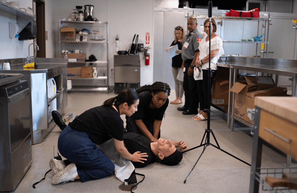 Two actors portray people helping administer Narcan to a chef in a kitchen