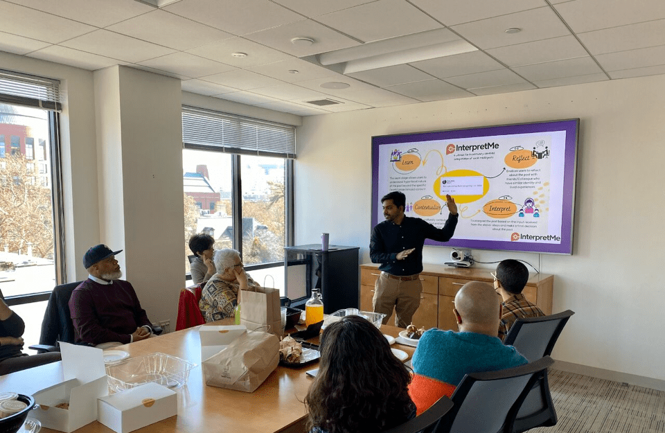 Prof. Siva Mathiyazhagan gives a presentation in front of a group of people sitting around a table in a conference room.