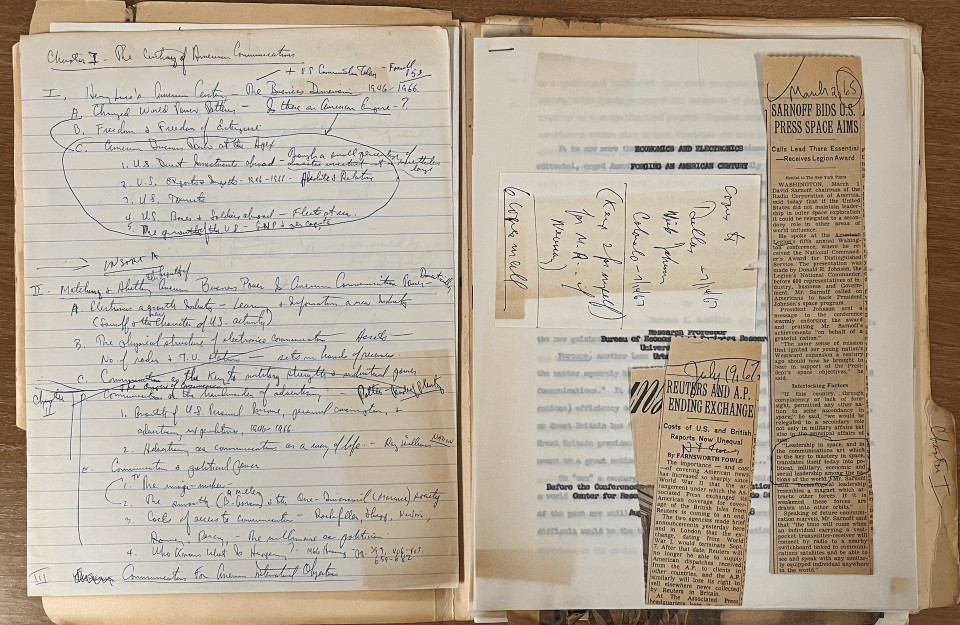 A open notebook with handwritten notes and pasted newspaper clips