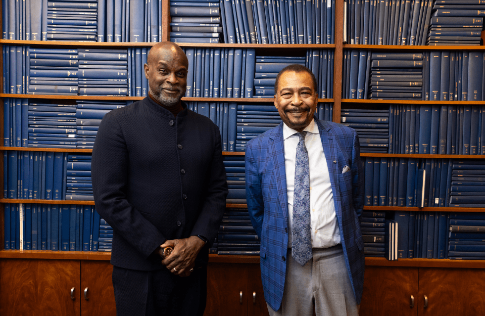 Tukufu Zuberi and Aldon Morris against a backdrop of blue hardback books stacked vertically and horizontally in a bookcase