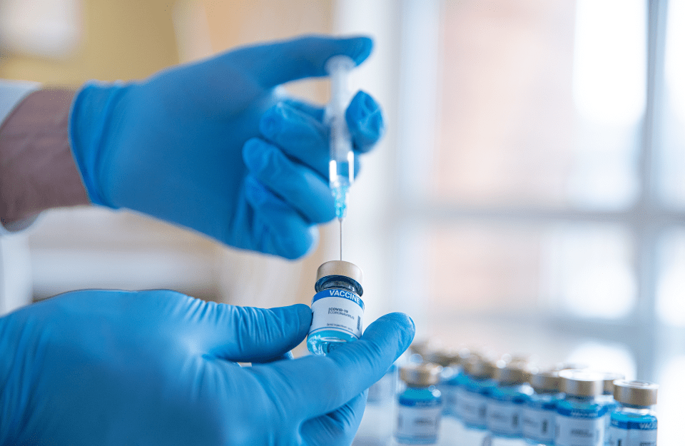 A person with gloved hands puts a needle into a vaccination vial  