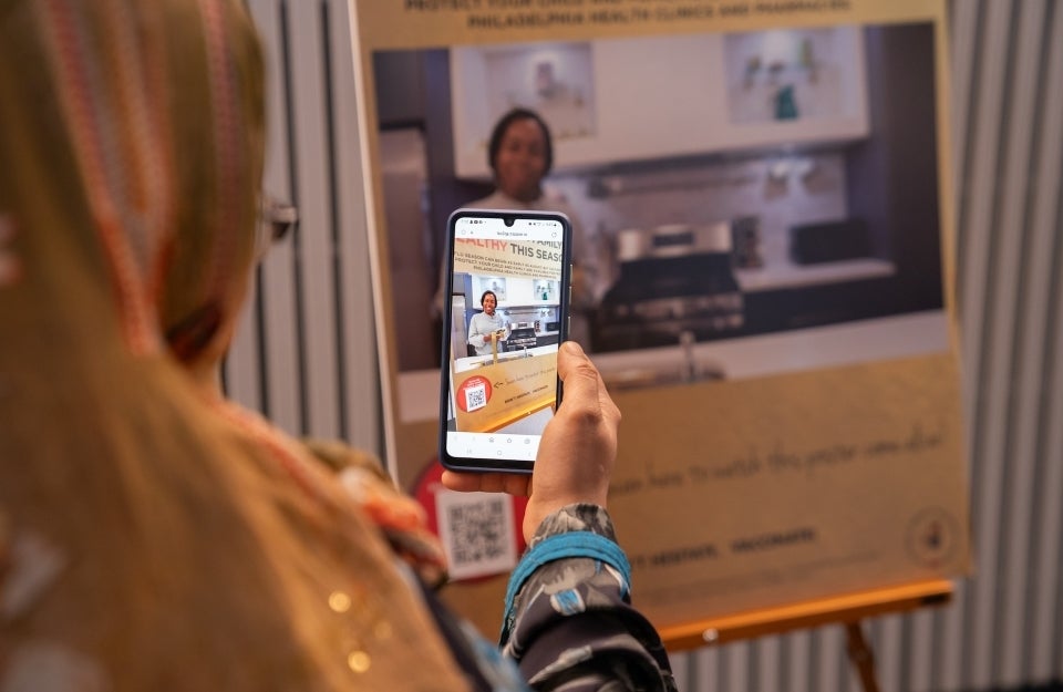 A person using a smartphone to watch a video on an informational poster at an event