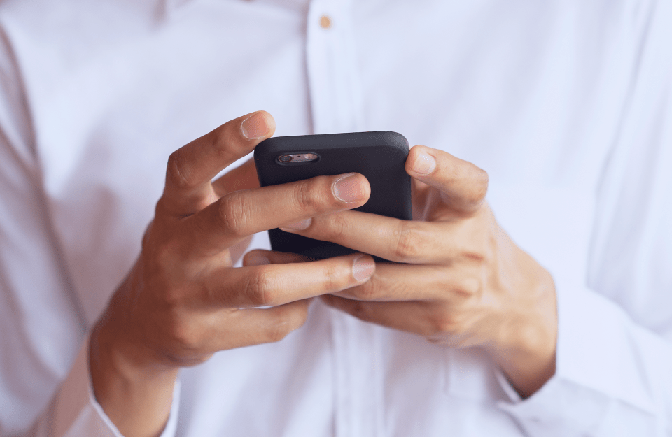 Close-up of a person in a white shirt using a smartphone.