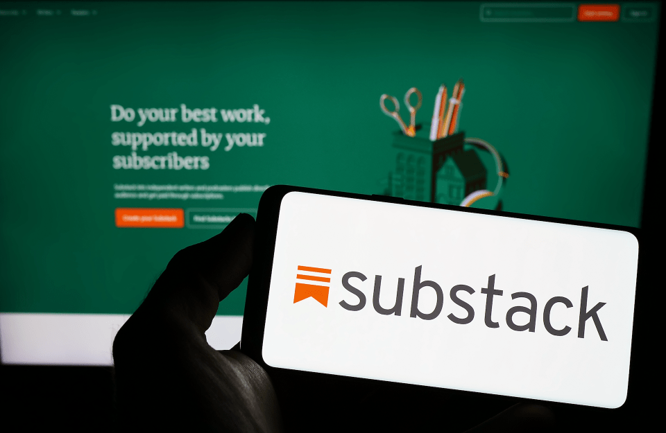 Person holding smartphone with the logo of US subscription company Substack in front of the pllatform's website. Focus on phone display.