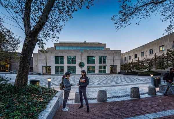 Two students in the foreground with the Annenberg Plaza and School building behind them