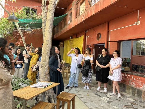 A group of people standing outside a terra cotta-colored building