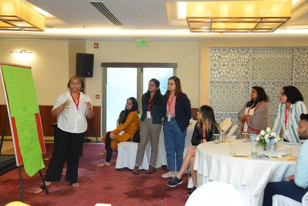 Woman stands at a large pad of paper and speaks to others who are seated around a hotel ballroom