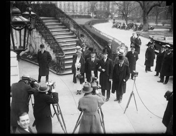 FDR arrives for his 1933 inauguration in a top hat, next to his wife Eleanor as media photographers in fedoras snap photos near the Capitol