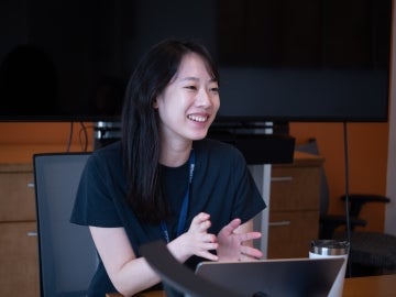 Youngrim Kim sits at a table with a laptop talking to someone offscreen